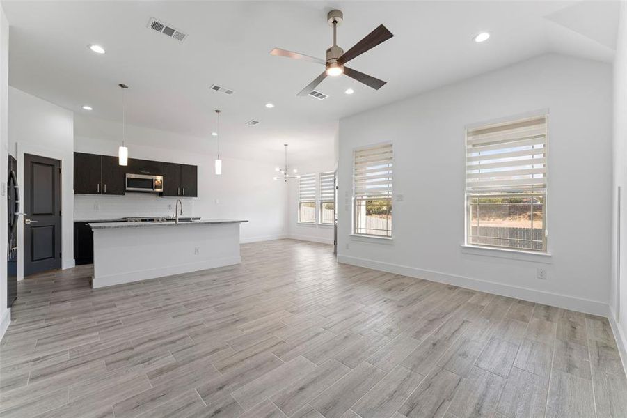 Unfurnished living room featuring ceiling fan with notable chandelier, light hardwood / wood-style floors, and sink