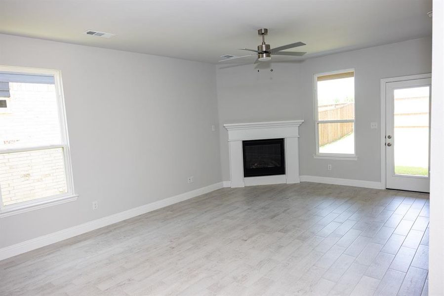 Unfurnished living room featuring light wood finished floors, a glass covered fireplace, and a ceiling fan Unfurnished living room featuring light wood finished floors, a glass covered fireplace, and a ceiling fan