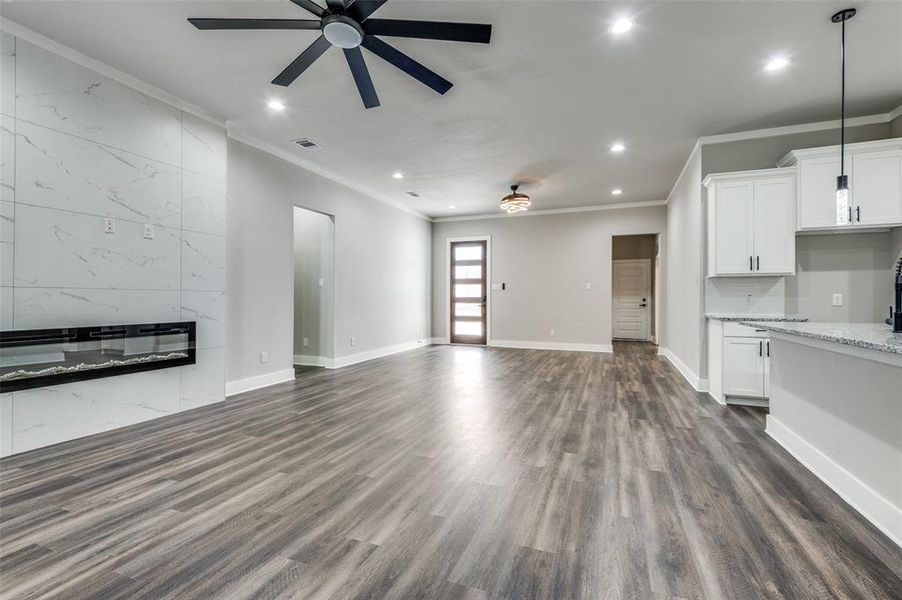 Unfurnished living room featuring ceiling fan, ornamental molding, recessed lighting, dark wood finished floors, and a fireplace Unfurnished living room featuring ceiling fan, ornamental molding, recessed lighting, dark wood finished floors, and a fireplace