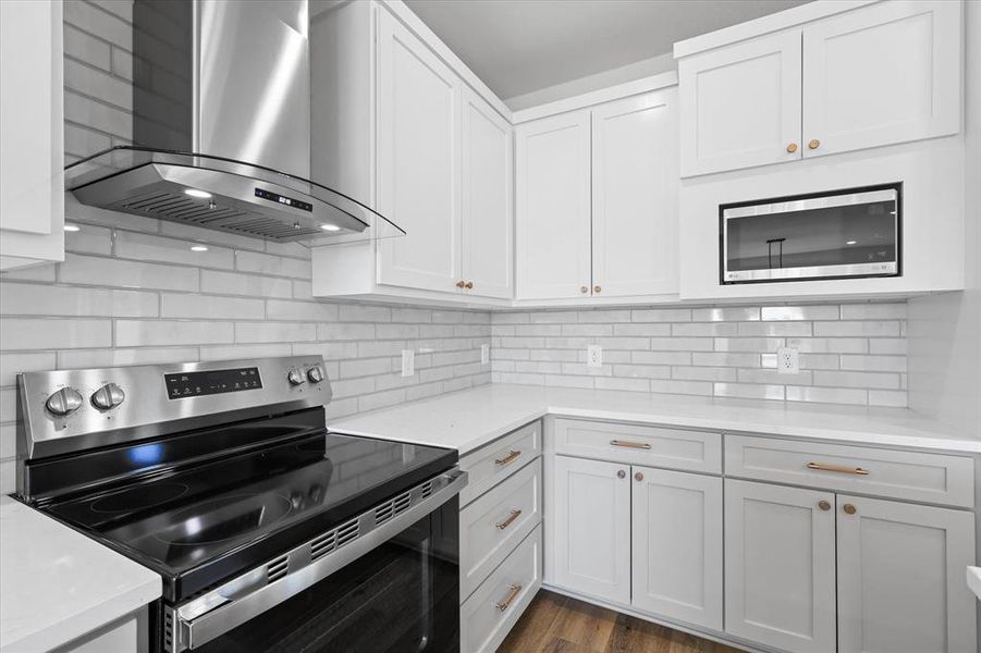 Kitchen with wall chimney exhaust hood, white cabinets, appliances with stainless steel finishes.