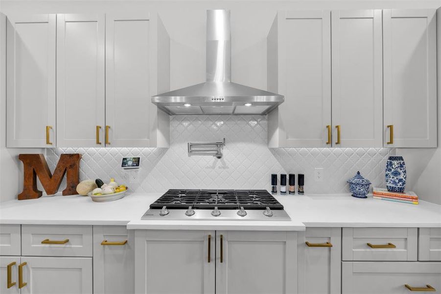 Kitchen featuring wall chimney exhaust hood, white cabinetry, gas cooktop, and tasteful backsplash