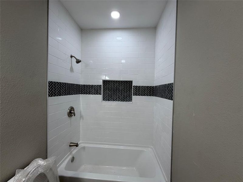 White subway tile bath surround with a black herringbone accent band and recessed niche