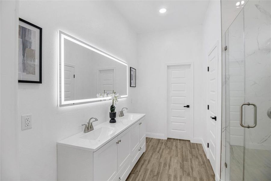 Bathroom with light wood-style flooring, double vanity, a marble finish shower, and recessed lighting Bathroom with light wood-style flooring, double vanity, a marble finish shower, and recessed lighting