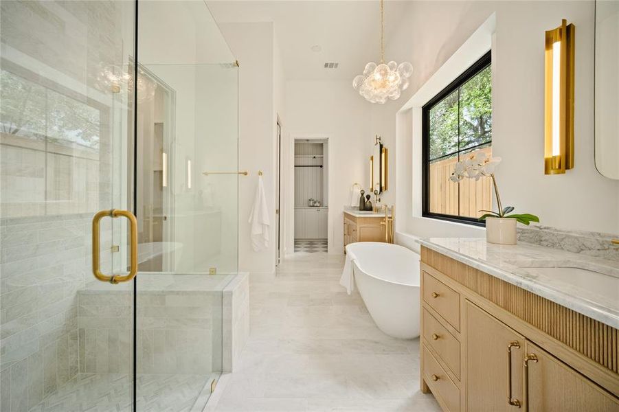 Bathroom featuring a stall shower, two vanities, a freestanding bath, and a chandelier
