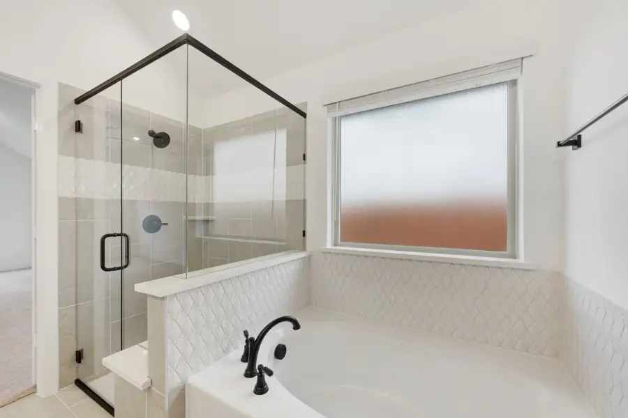 Bathroom with glass-enclosed tile shower, soaking tub, black fixtures, and frosted window