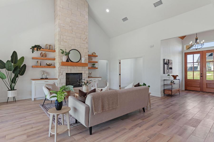 Living area with light wood-type flooring, french doors, hanging lights, vaulted ceiling, and a stone fireplace Living area with light wood-type flooring, french doors, hanging lights, vaulted ceiling, and a stone fireplace