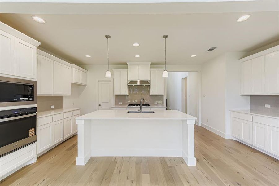 Kitchen with decorative backsplash, appliances with stainless steel finishes, hanging light fixtures, recessed lighting, and light wood finished floors Kitchen with decorative backsplash, appliances with stainless steel finishes, hanging light fixtures, recessed lighting, and light wood finished floors
