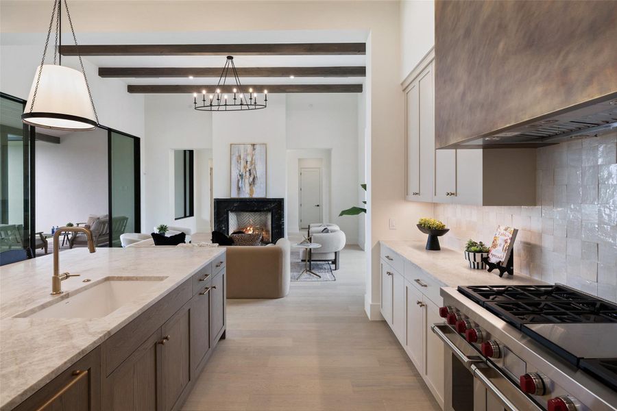 Kitchen featuring a warm lit fireplace, high end stainless steel range oven, a sink, light stone countertops, and wall chimney exhaust hood Kitchen featuring a warm lit fireplace, high end stainless steel range oven, a sink, light stone countertops, and wall chimney exhaust hood