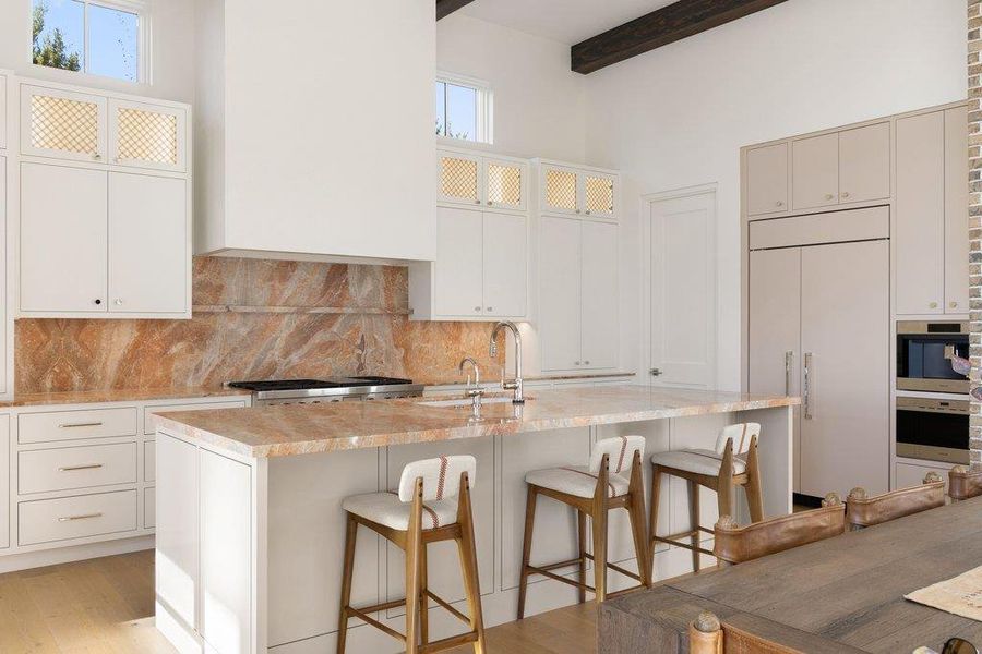 Kitchen featuring glass fronted cabinets, paneled refrigerator, light wood-style flooring, a kitchen breakfast bar, and an island with sink
