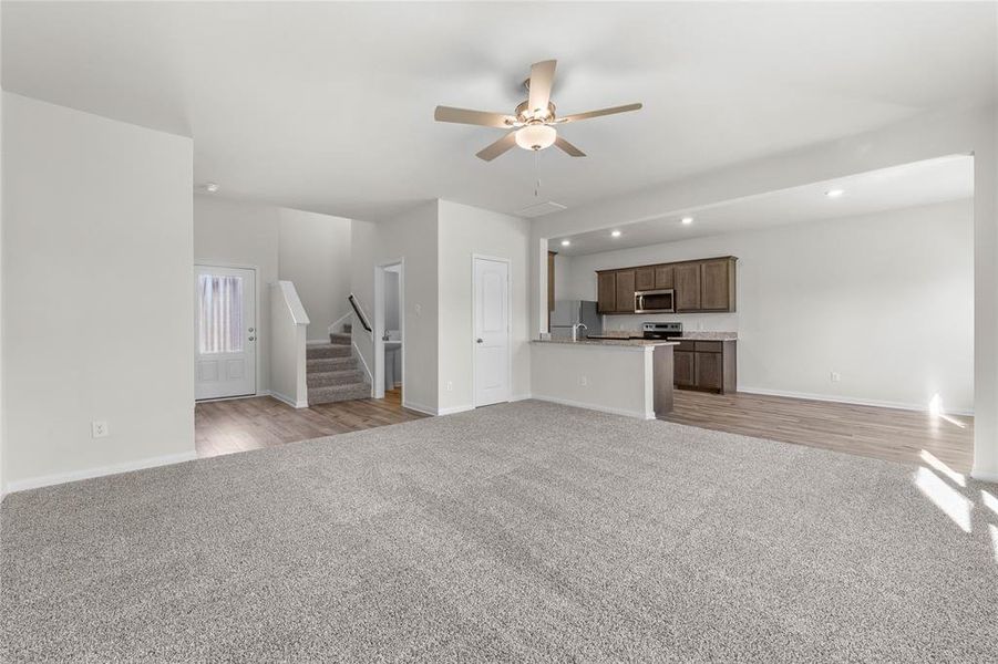 Unfurnished living room with recessed lighting, light colored carpet, a ceiling fan, baseboards, and stairs