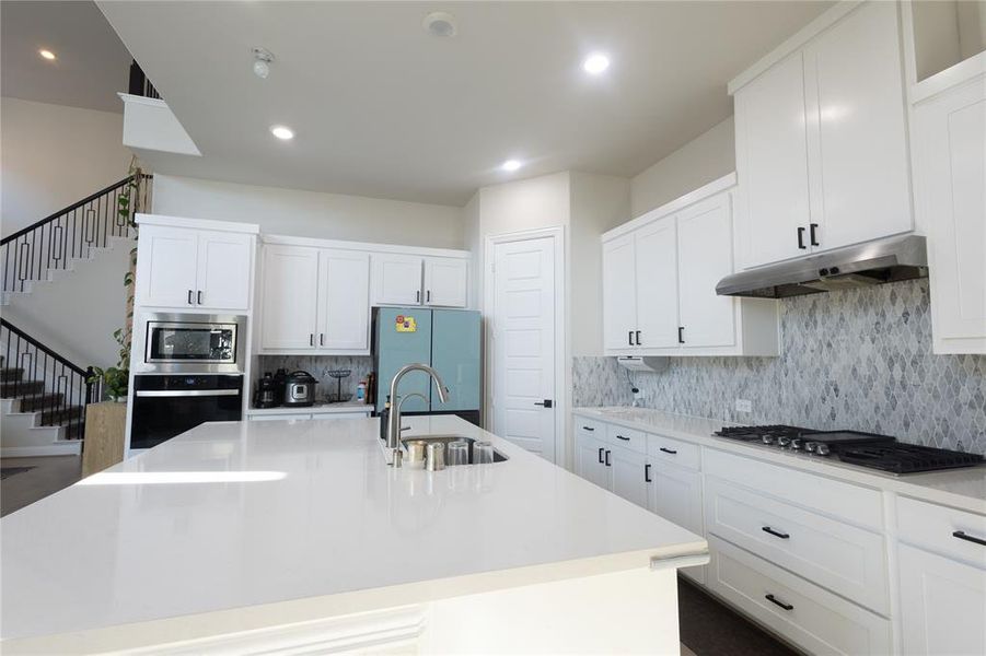 Kitchen with white cabinets, appliances with stainless steel finishes, light stone counters, a kitchen island with sink, and recessed lighting