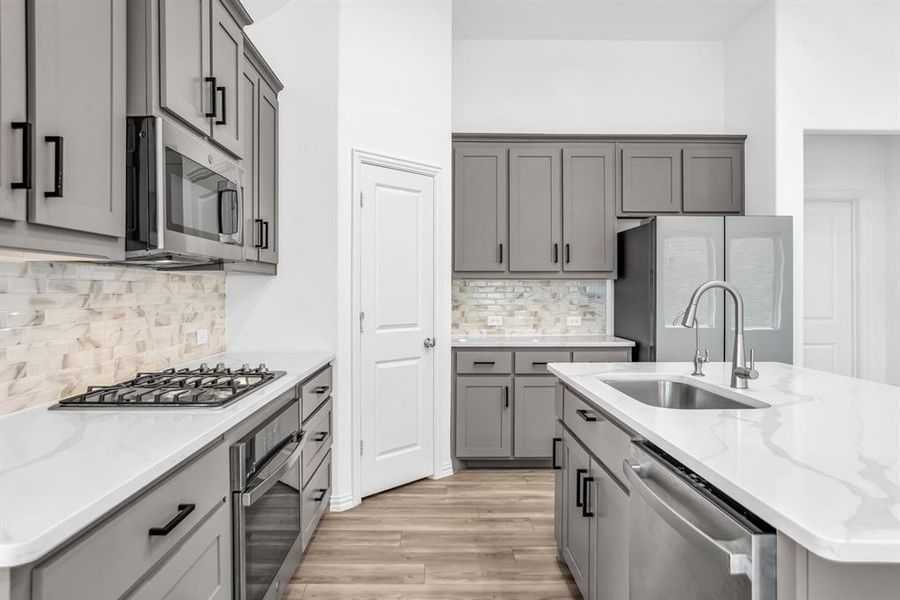 Contemporary kitchen featuring grey cabinetry with matte black hardware, white countertops, and a full tile backsplash