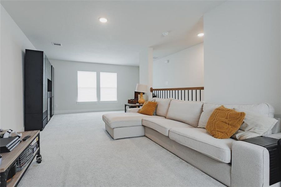 Carpeted loft space featuring dual windows, recessed lighting, and a wood-finish railing with black metal spindles
