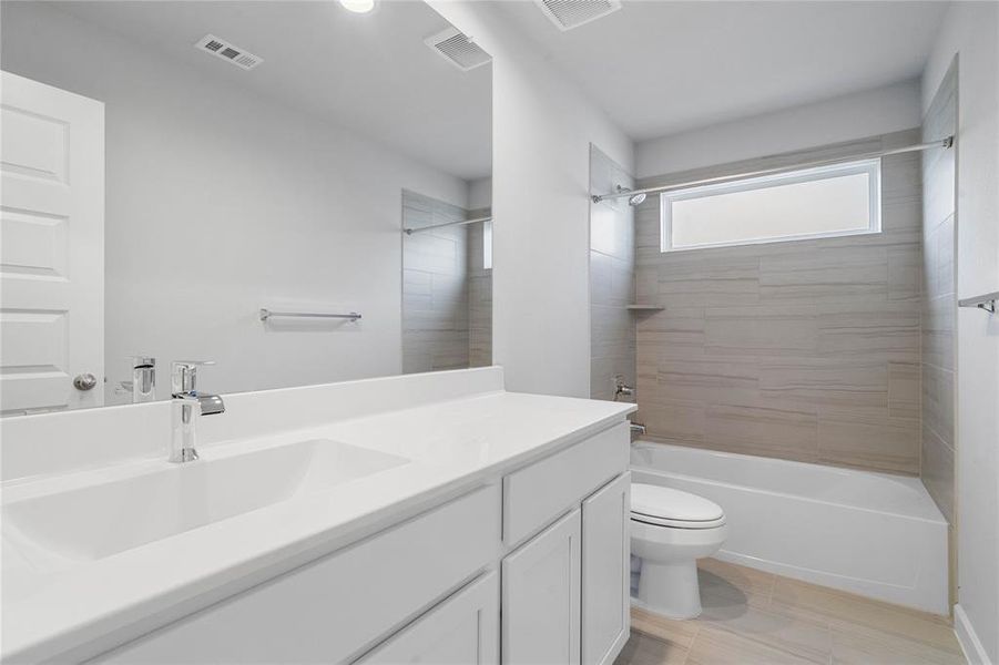 Secondary bath features tile flooring, bath/shower combo with tile surround, stained wood cabinets, beautiful light countertops, mirror, sleek fixtures and modern finishes.