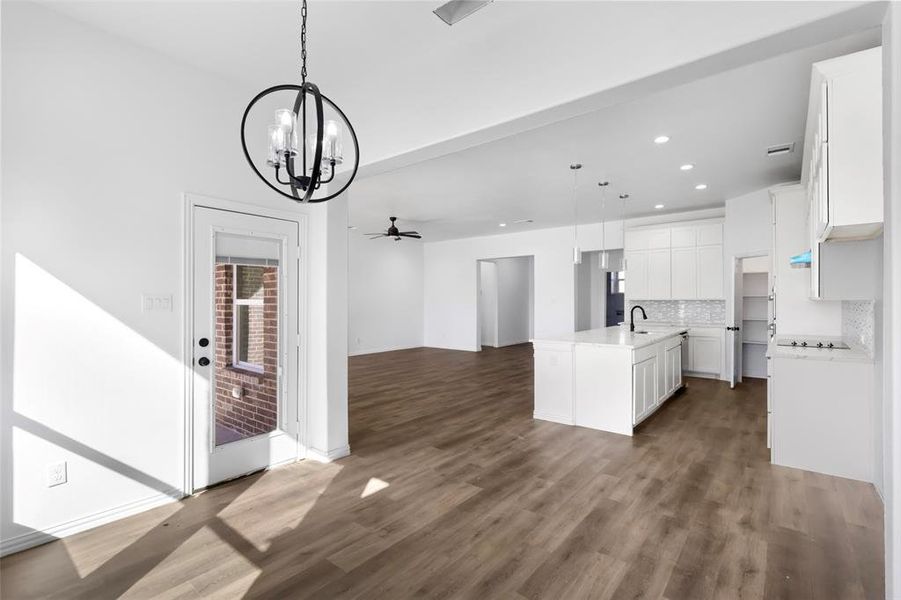 Kitchen with sink, hanging light fixtures, backsplash, a kitchen island with sink, and white cabinets