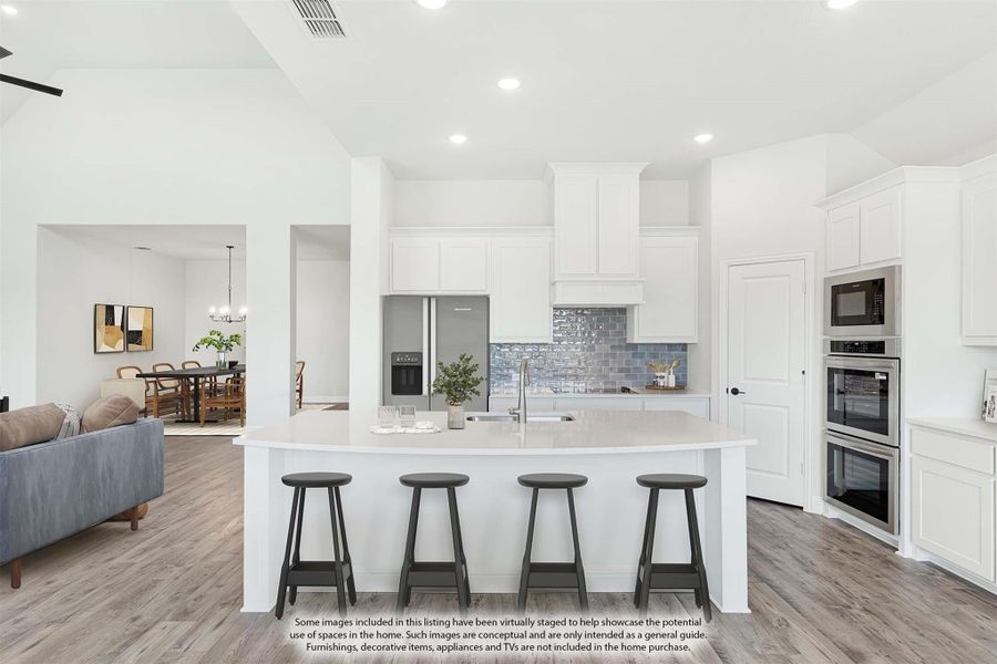 Open kitchen with large white island, four bar stools, white cabinets, blue tile backsplash, and stainless steel appliances