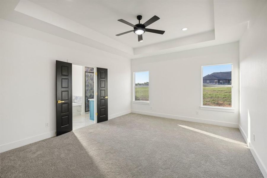 Unfurnished bedroom featuring carpet floors, ensuite bath, a raised ceiling, and ceiling fan