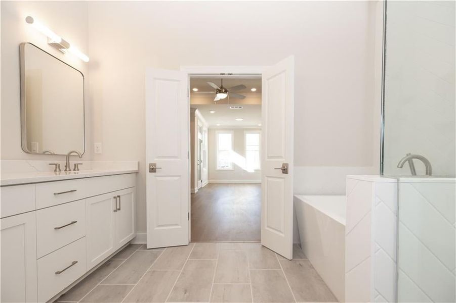 Primary bathroom with a free-standing soaking tub, double vanity with accented framed mirrors, upgrading lighting and tile floors. Image is of a previously built Chamberlain Plan