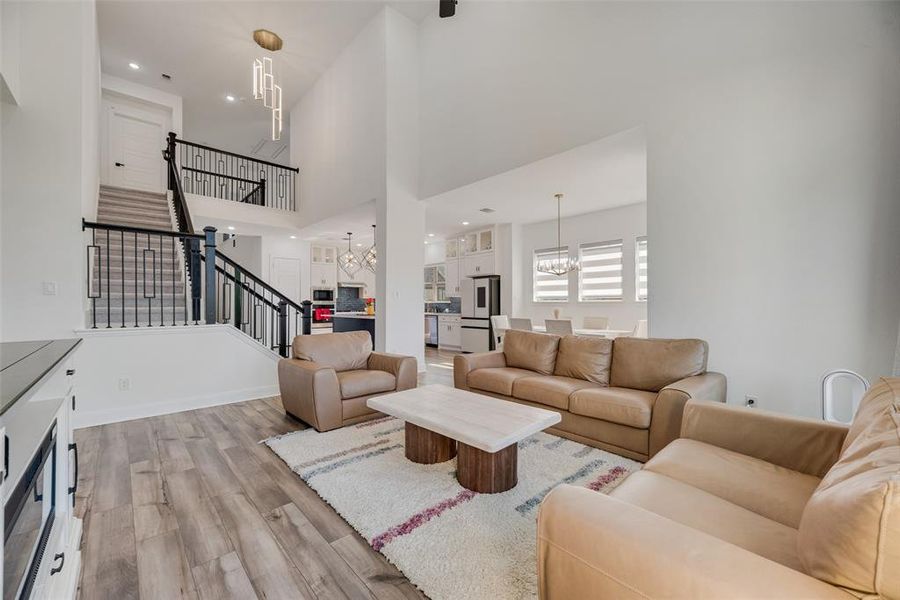 Living room with a chandelier, a high ceiling, light wood-type flooring, recessed lighting, and stairway