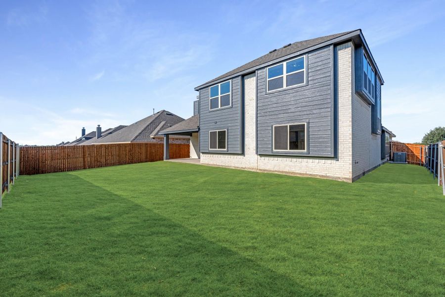Two-story home with gray siding and brick base, large fenced backyard with green lawn Two-story home with gray siding and brick base, large fenced backyard with green lawn
