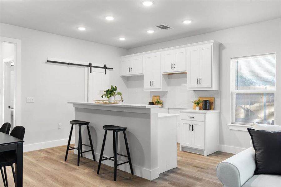 Kitchen featuring a barn door, a breakfast bar, white cabinetry, visible vents, and a center island