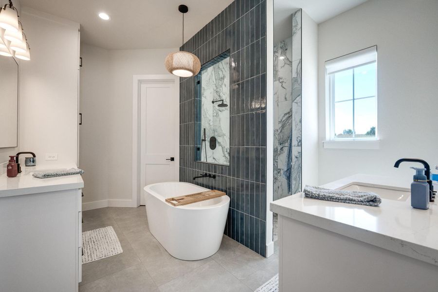 Full bath with two vanities, walk in shower, a soaking tub, and light tile patterned flooring
