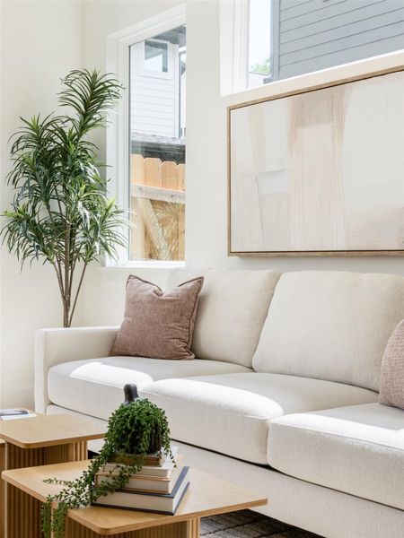 Sunlit interior featuring a large window, white walls, and a light-colored sectional sofa