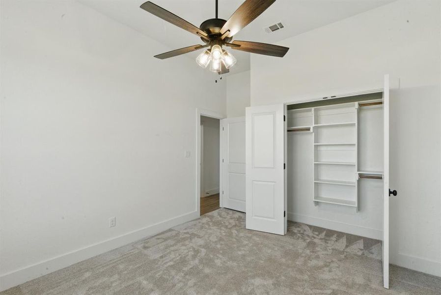 Unfurnished bedroom featuring light carpet, a closet, a ceiling fan, and a high ceiling Unfurnished bedroom featuring light carpet, a closet, a ceiling fan, and a high ceiling