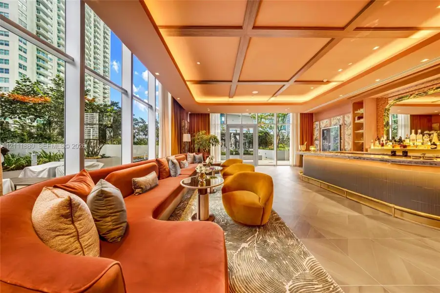 Floor-to-ceiling windows, recessed coffered ceiling with perimeter lighting, geometric tile flooring, and a stone-topped bar with metallic accents