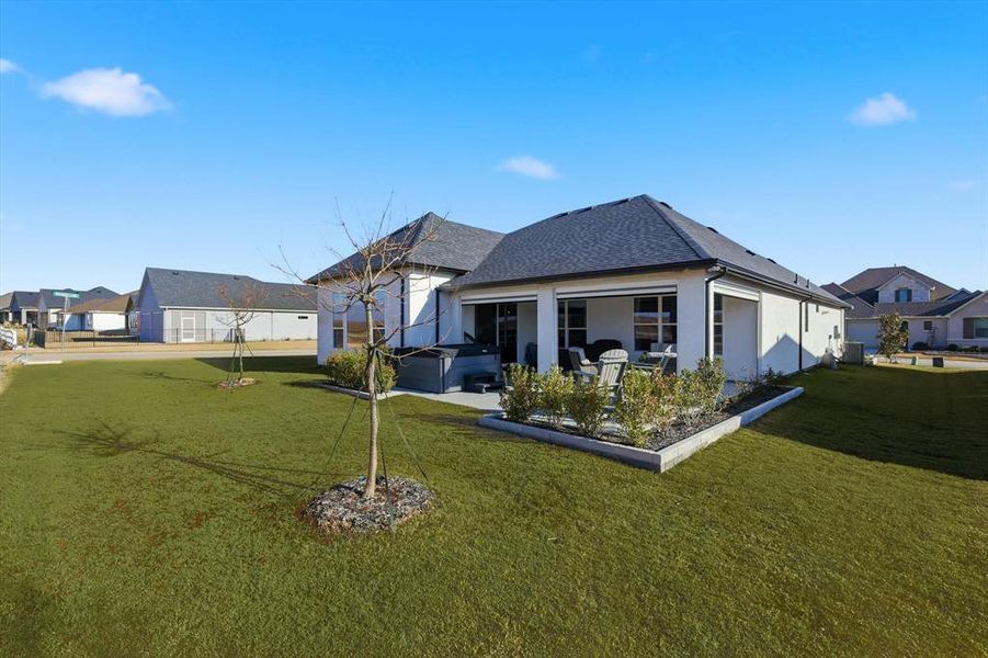 Back of property featuring a yard, stucco siding, a shingled roof, and a hot tub