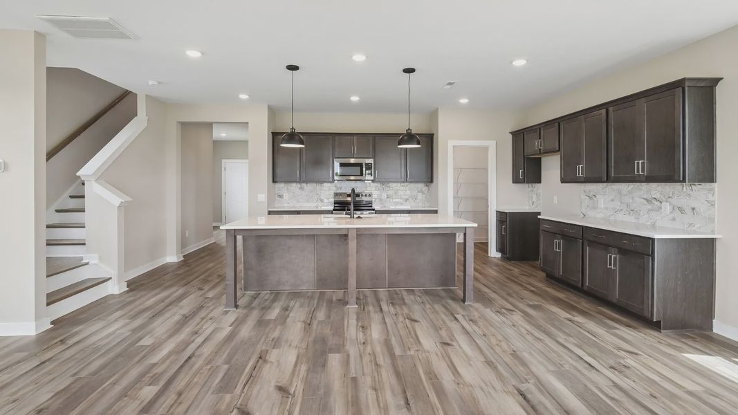 Kitchen with dark cabinetry, quartz countertops, and tile backsplash with nearby staircase Kitchen with dark cabinetry, quartz countertops, and tile backsplash with nearby staircase