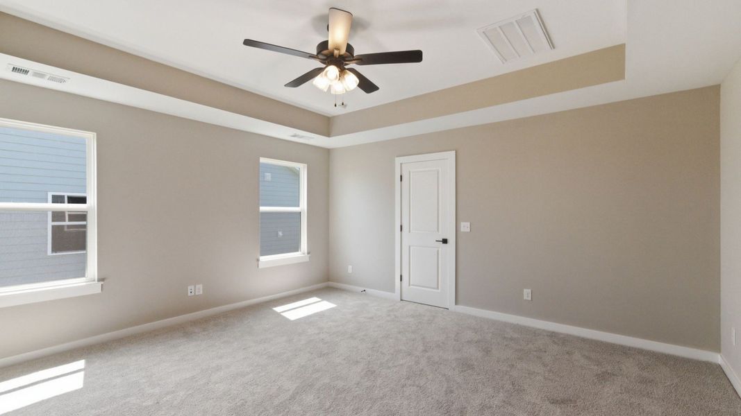 Primary suite with tray ceiling, ceiling fan, and carpet