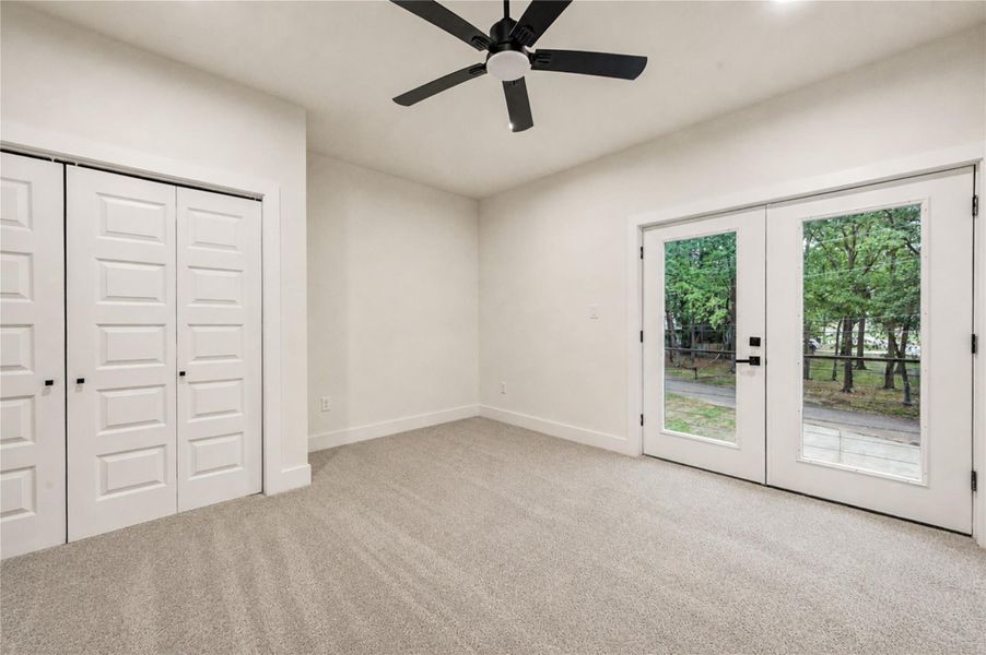 Bright and spacious 3rd bedroom with plush carpeting, featuring double French doors that open to a scenic outdoor view, complemented by a modern ceiling fan and ample closet space.