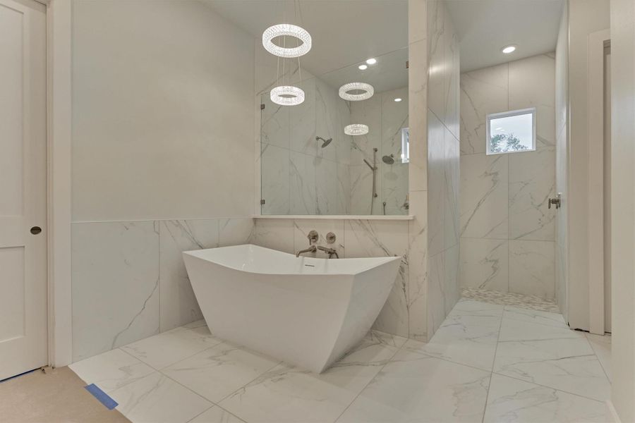 Spa-inspired retreat featuring a sculptural freestanding tub, luxe marble-look tile, and a seamless walk-in shower framed by modern pendant lighting.