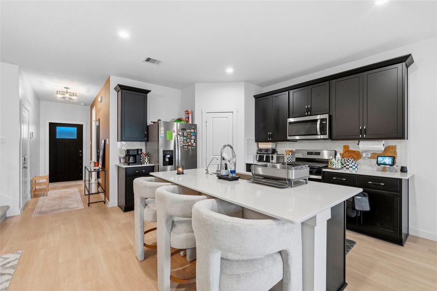 From this perspective, the kitchen showcases a generous island with seating, paired with elegant dark cabinetry, stainless steel appliances, and a refined, modern backsplash. From this perspective, the kitchen showcases a generous island with seating, paired with elegant dark cabinetry, stainless steel appliances, and a refined, modern backsplash.