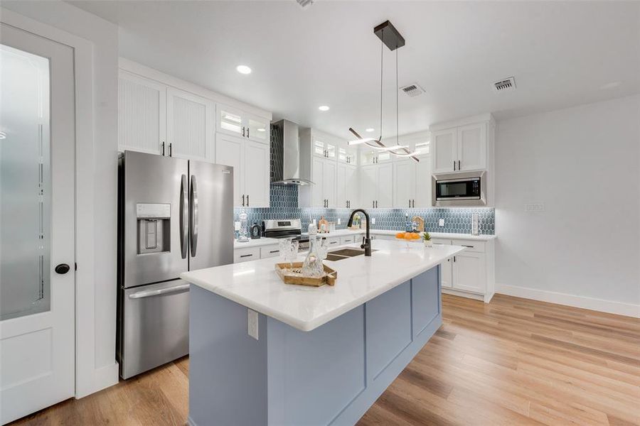 Kitchen with decorative light fixtures, a center island with sink, stainless steel appliances, sink, and wall chimney range hood