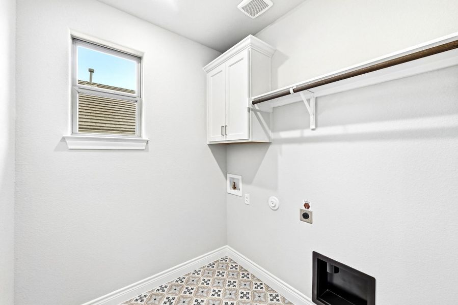 Laundry room featuring patterned floor tile, a single window, white upper cabinetry, and an integrated shelf with hanging rod
