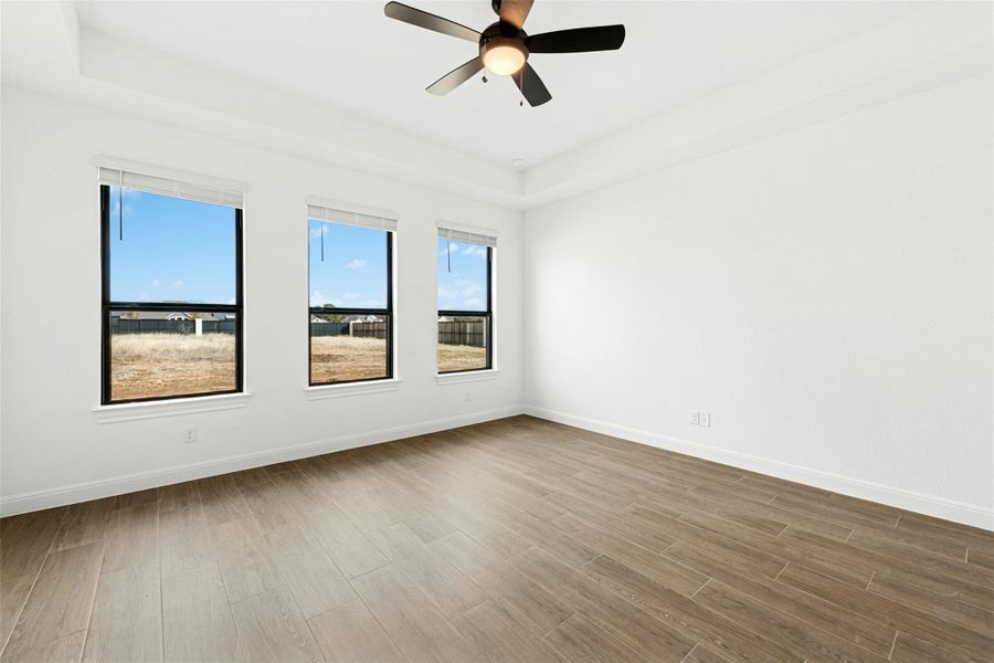 Empty room with wood finished floors, a tray ceiling, and a ceiling fan