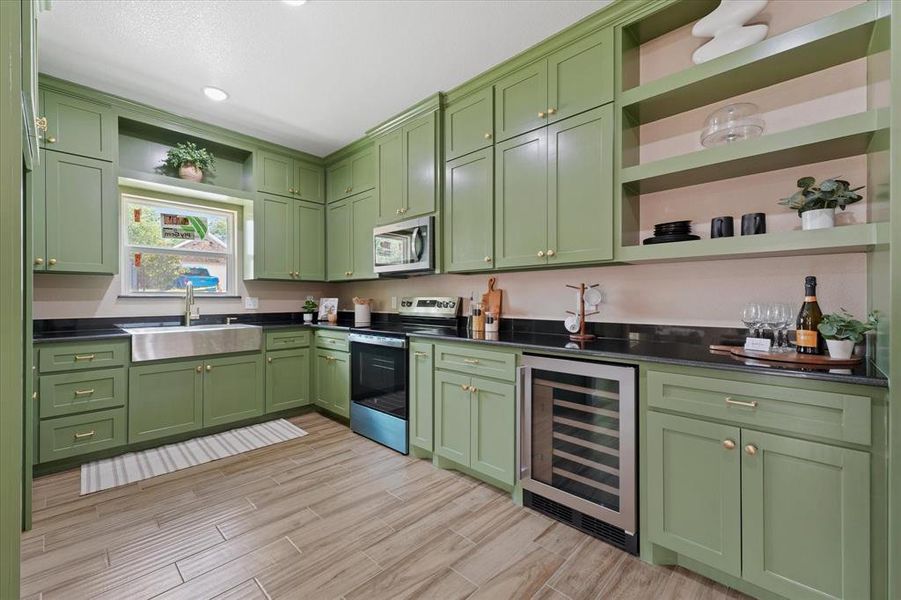 Kitchen featuring open shelves, green cabinets, wine cooler, appliances with stainless steel finishes, and wood finish floors Kitchen featuring open shelves, green cabinets, wine cooler, appliances with stainless steel finishes, and wood finish floors