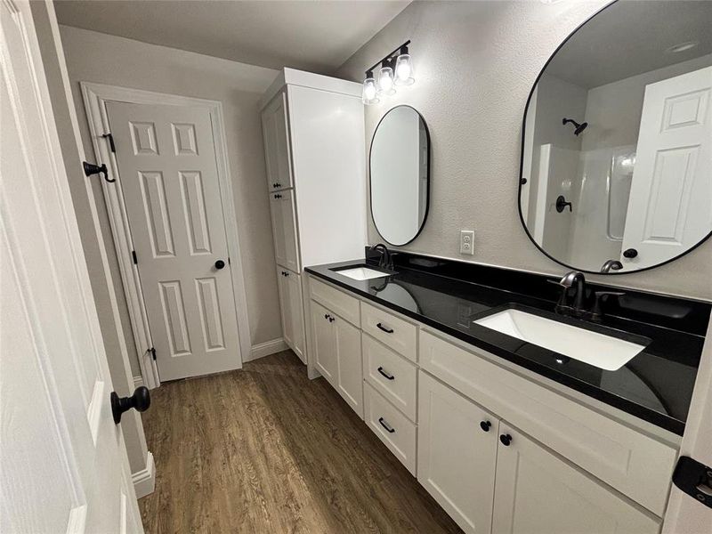 Full bathroom with double vanity, dark wood-style flooring, and a shower