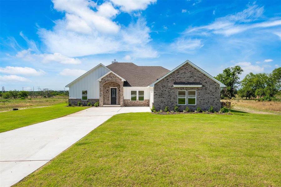 View of front of home featuring board and batten siding, a front lawn, driveway, and brick siding