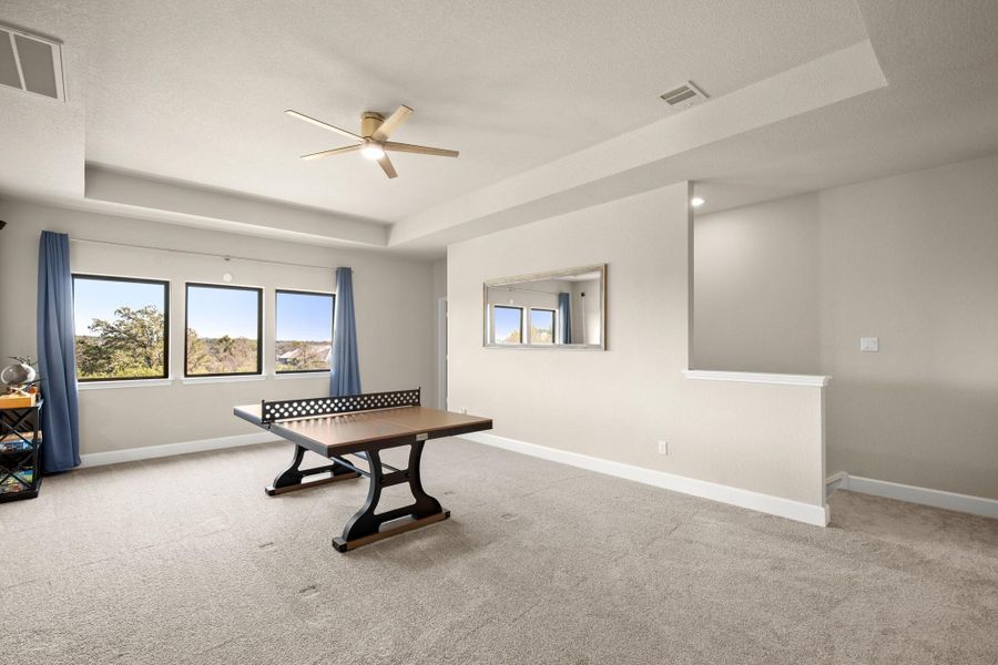 Recreation room with a tray ceiling, light colored carpet, a ceiling fan, and a textured ceiling Recreation room with a tray ceiling, light colored carpet, a ceiling fan, and a textured ceiling