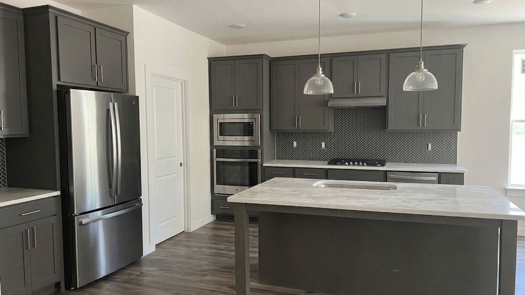 Kitchen with quartz countertops, island, pantry, appliances, and tile backsplash