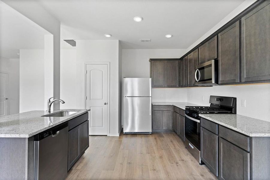 Kitchen featuring sink, light wood-style flooring, light stone countertops, and stainless steel appliances