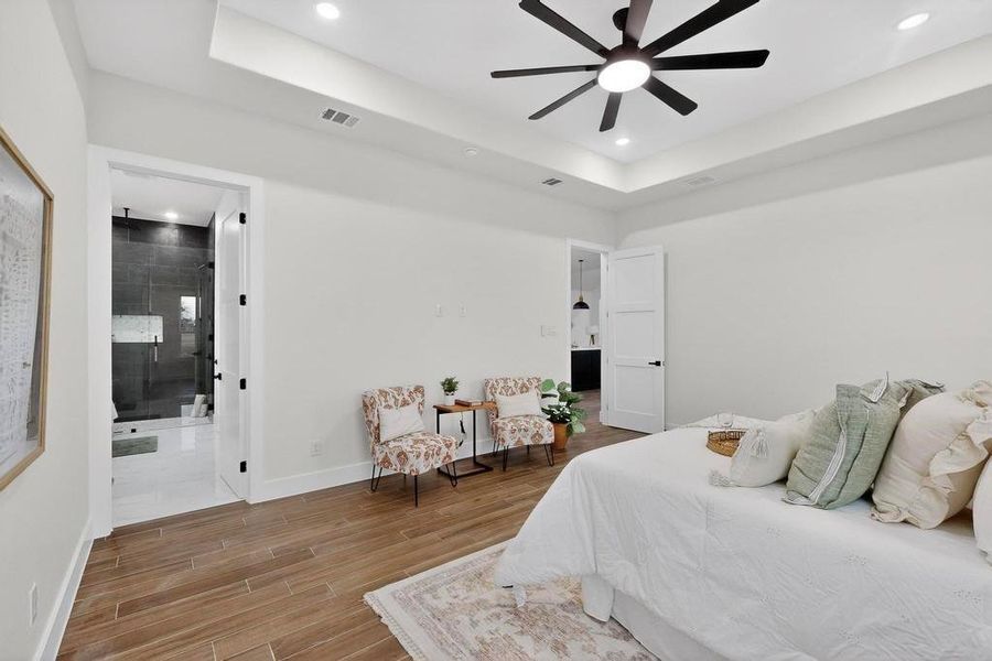 Primary Bedroom with a raised ceiling, wood tiled floors, recessed lighting, a ceiling fan, and ensuite bath Primary Bedroom with a raised ceiling, wood tiled floors, recessed lighting, a ceiling fan, and ensuite bath