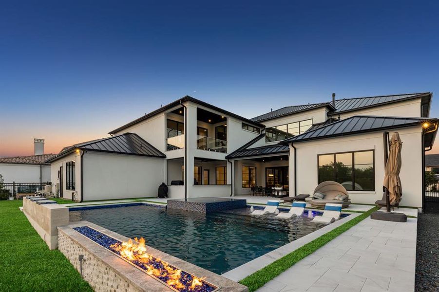 Back house at dusk with a balcony, a fenced in pool, a patio, and a fire pit