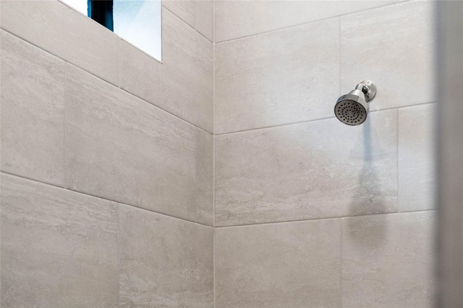 The fixed shower head and arm assembly feature a warm-toned, metallic finish. This finish adds a luxurious, modern accent that contrasts beautifully with the tile.