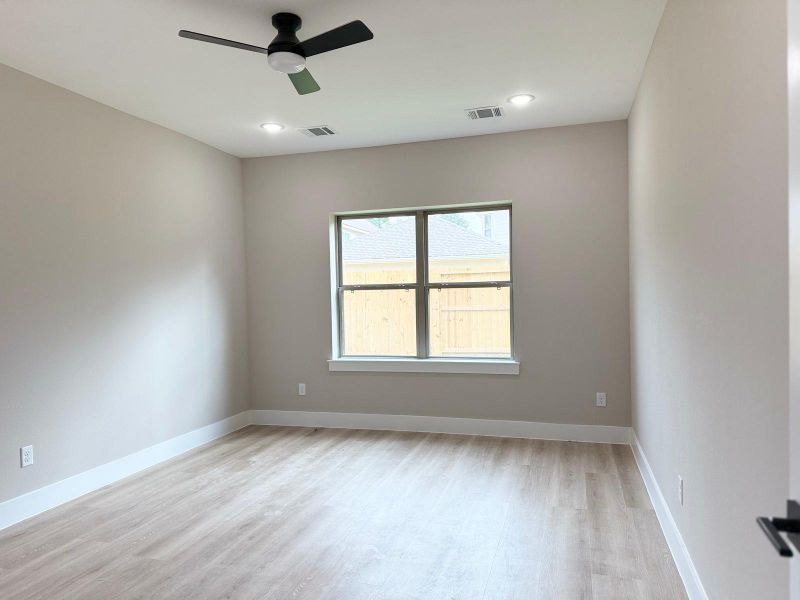 Spacious primary bedroom with abundant natural light, sleek ceiling fan, and elegant wood flooring. Perfect for relaxation and comfort.