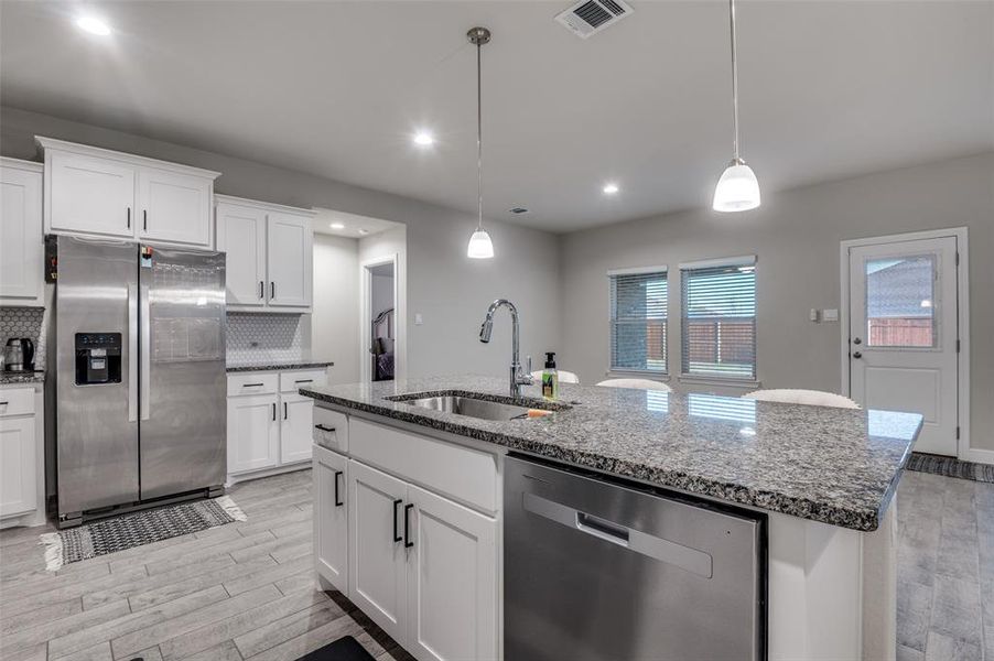 Kitchen with stainless steel appliances, light wood-type flooring, dark stone countertops, and white cabinetry
