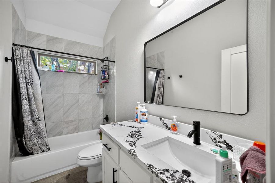 Bathroom featuring shower / tub combo, vanity, a textured wall, and vaulted ceiling